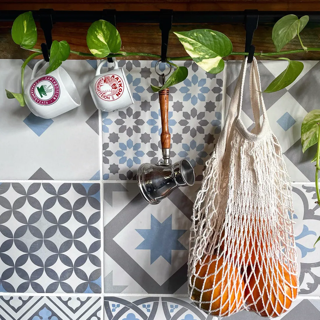 Enamel mugs and net bag of oranges on patterned tiles